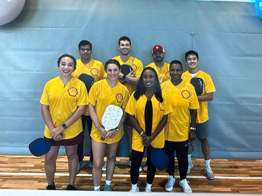 A team in matching yellow jerseys posing with pickleball paddles on an indoor court