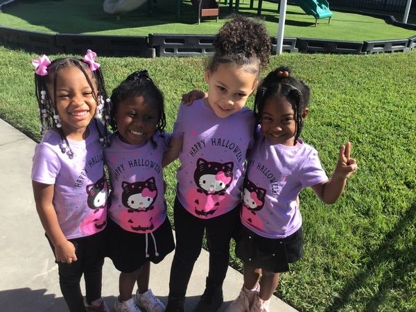 Four girls in matching lavender shirts smiling together at a school supply drive